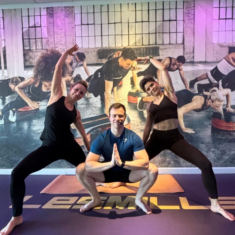 Drei Yogatrainer in Yogaposen auf der Bühne, zwei Frauen, ein Mann