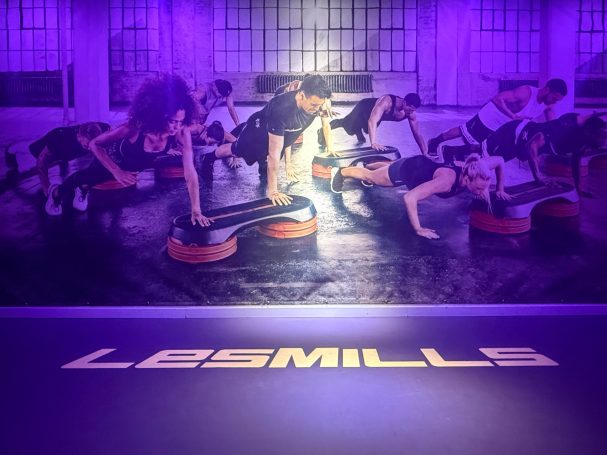 beleuchtete Bühne mit Les Mills Schriftzug und großem Poster an der Wand