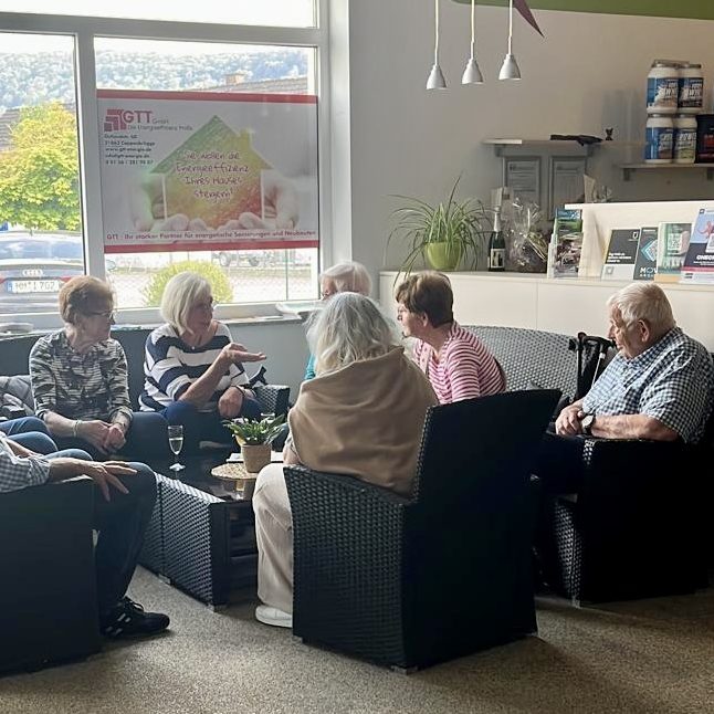 7 ältere Mitglieder sitzen gemütlich in einer Sitzecke und trinken Kaffee und unterhalten sich