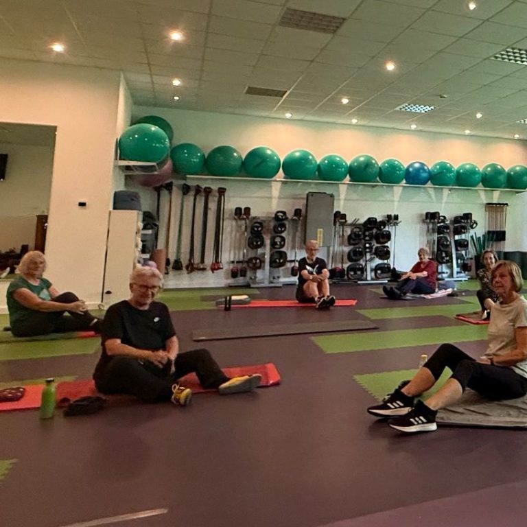 Kursraum mit Rehasportteilnehmern, die auf den Matten sitzen