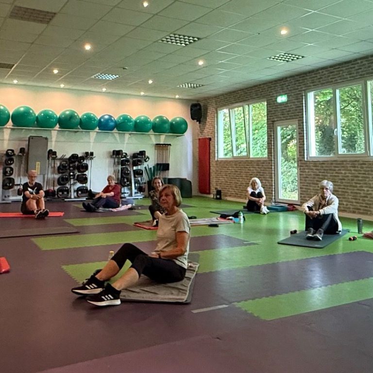 Kursteilnehmer:innen auf den Matten sitzend im Kursraum