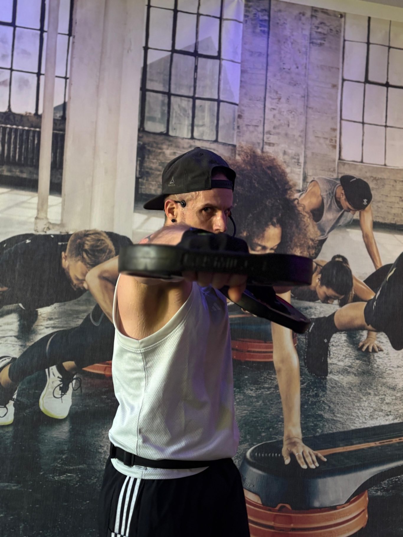 Trainer im Kurs mit Gewichtsscheiben auf Schulterhöhe, Mac raise