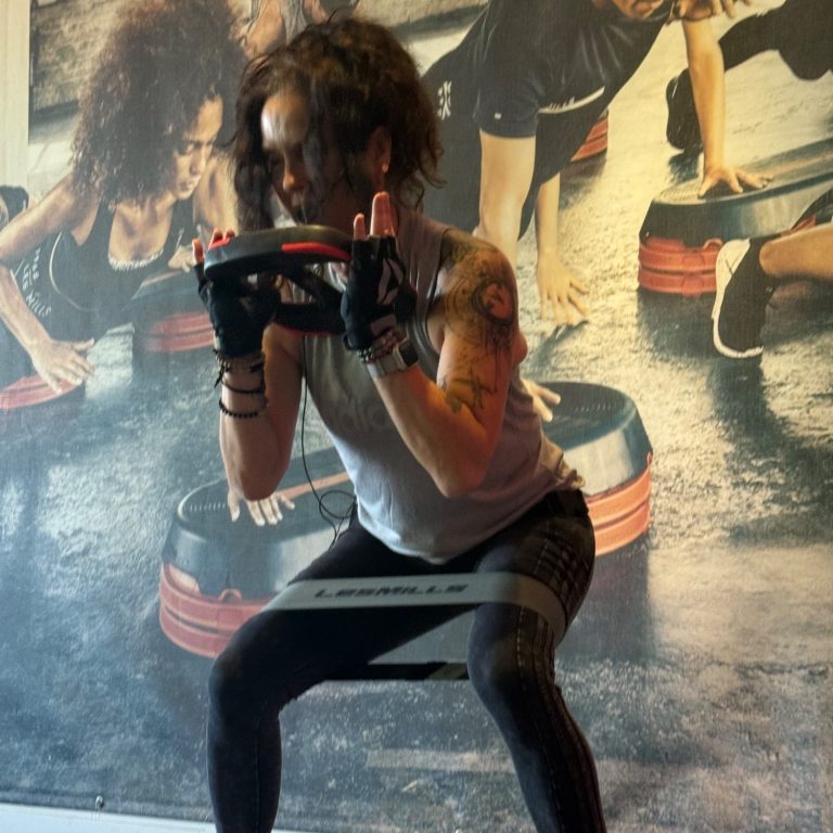 Trainerin im Kurs mit Widerstandsband an den Beinen und Gewichtsscheibe in den Händen