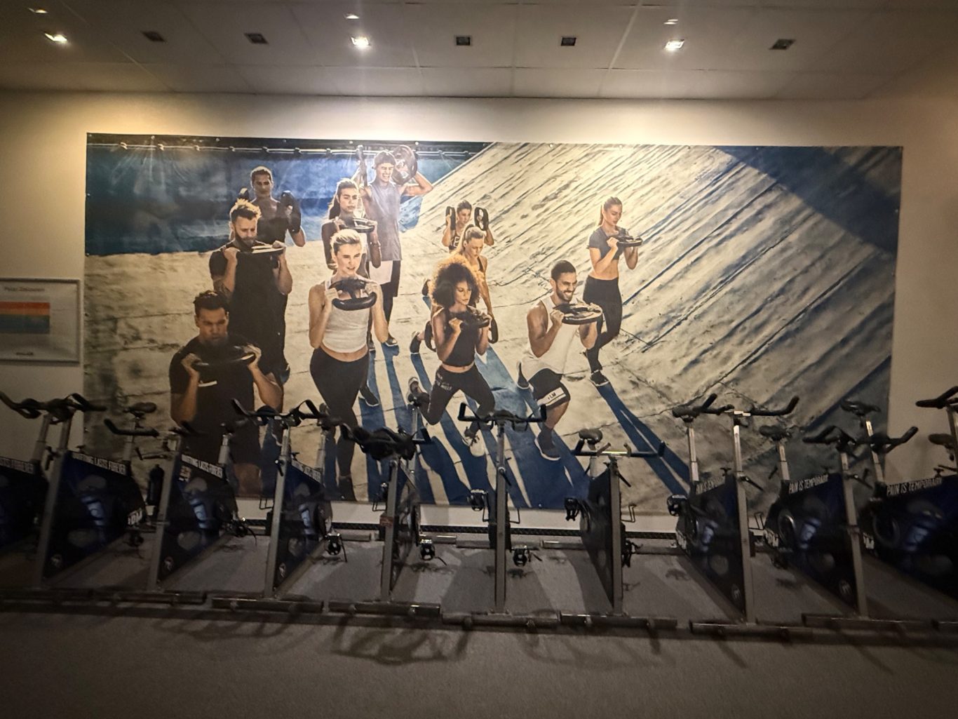 Mehrere Spinnig Räder vor einer Wand mit großem Bild mit trainierenden Menschen